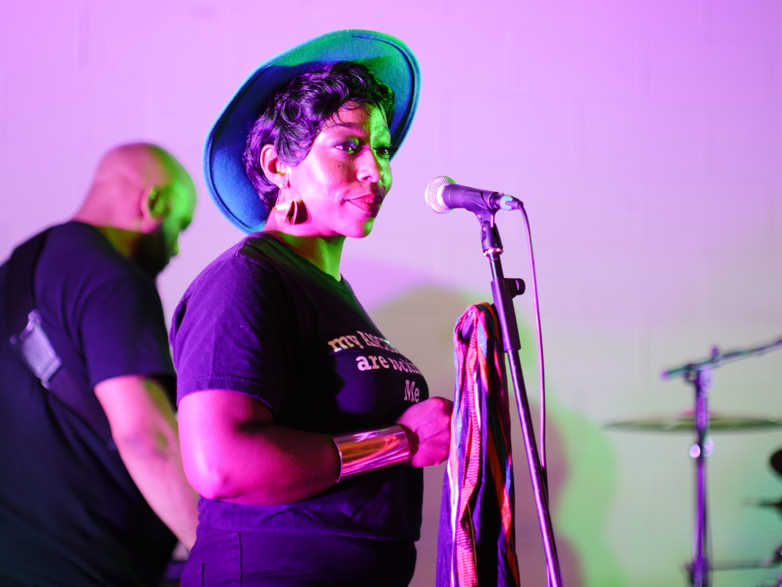 Musician wearing hat stands on stage at microphone during Concert series.