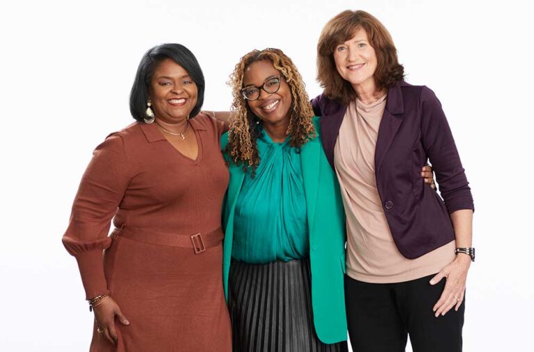 Three women pose for photo together, smiling at the camera.