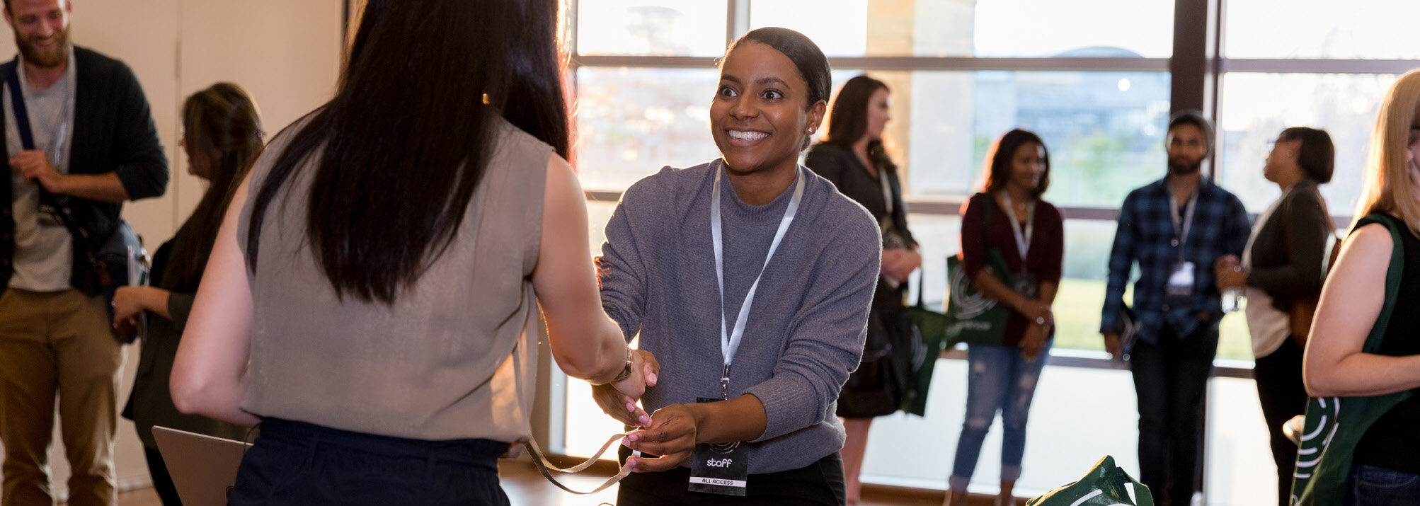Two women on either side of a table shake hands as they meet at a health conference.